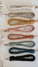 Load image into Gallery viewer, Natural White, oatmeal, mustard yellow, blush pink, terra cotta, laurel, peacock blue, and black macrame wristlet keychain and their respective names
