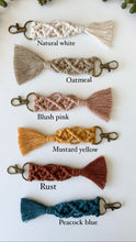 Load image into Gallery viewer, Six  6-inch macrame keychains with gold keychain ring and clasp seen in natural white, oatmeal, mustard yellow, rust, and peacock blue cotton with respective color names 
