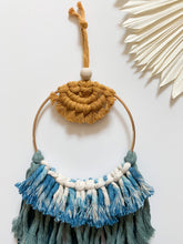 Load image into Gallery viewer, A macrame wall hanging with mustard colored cotton cord to reflect a sunset and a mix of blue toned cotton cord fringe hand tied to a golden hoop 
