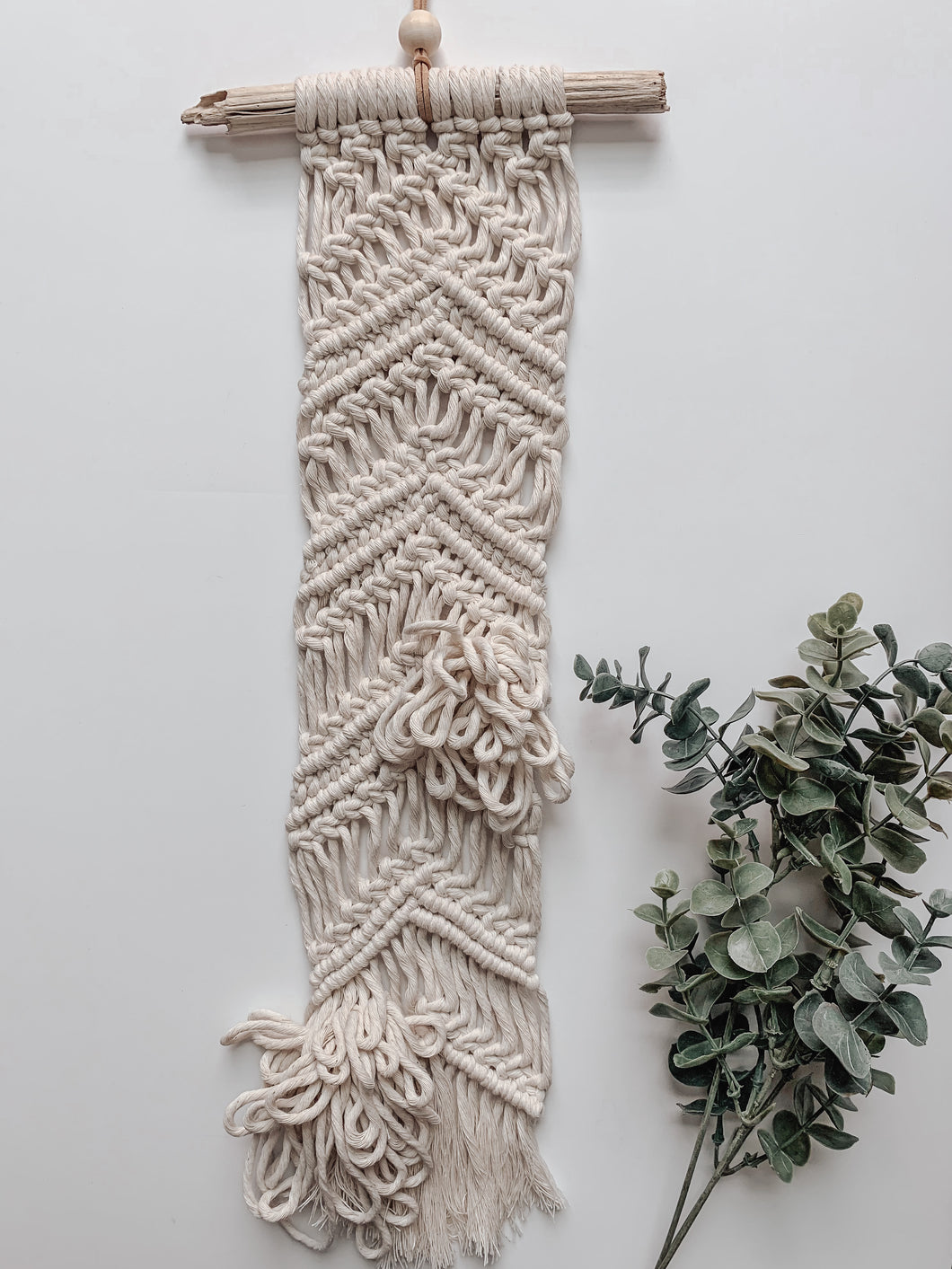 A natural white vertical macrame wall hanging with cotton cord hand knotted on driftwood