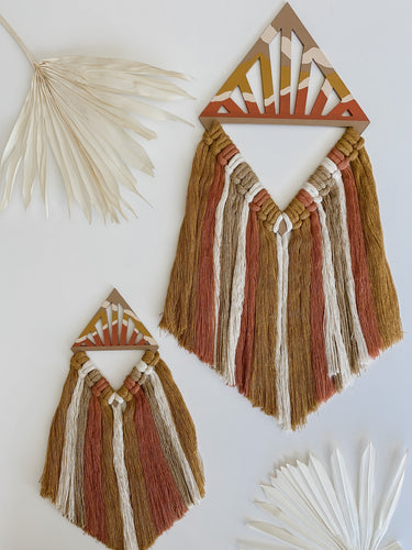 A set of two diamond shaped macrame wall hangings made of terra cotta, mustard yellow, and white colored cotton cord tassels hand knotted on wood cut outs