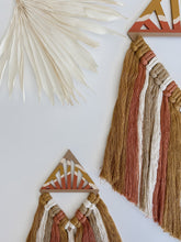 Load image into Gallery viewer, A diamond shaped macrame wall hanging made of terra cotta, mustard yellow, and white colored cotton cord tassels hand knotted on a wood cut out

