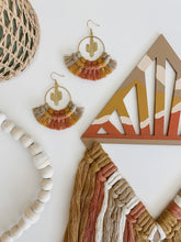Load image into Gallery viewer, A diamond shaped macrame wall hanging made of terra cotta, mustard yellow, and white colored cotton cord tassels hand knotted on a wood cut out
