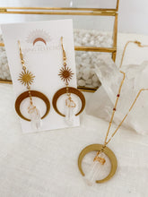 Load image into Gallery viewer, A pair of drop earrings with raw brass crescent and clear quartz charm seen on packaging
