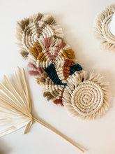 Load image into Gallery viewer, A natural white macrame coaster, a beige mixed with white macrame coaster, a white, pink, and yellow macrame coaster, and a beige, blue, and terra cotta macrame coaster
