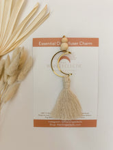 Load image into Gallery viewer, A gold crescent moon charm with cotton tassels shown on packaging
