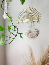 Load image into Gallery viewer, A macrame sun catcher with gold crescent charm and fringe detailing hanging on a wall hook
