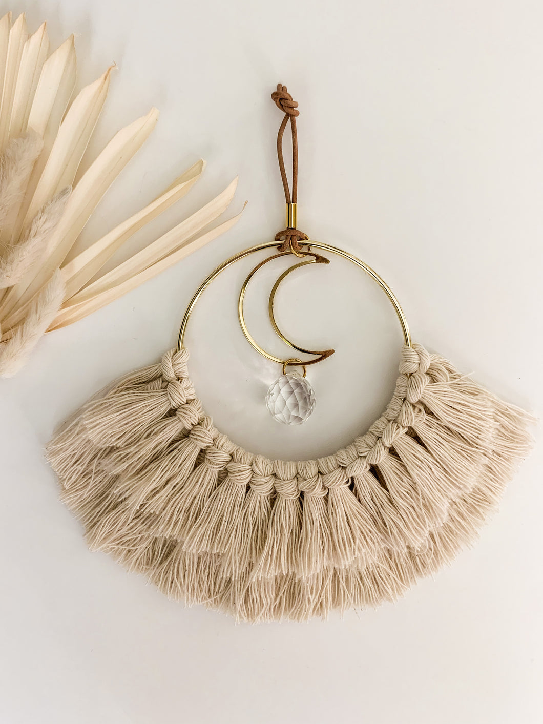 A macrame sun catcher with gold crescent charm and fringe detailing