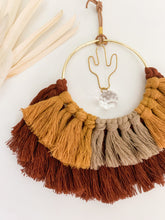 Load image into Gallery viewer, A macrame suncatcher with gold cactus charm and mix of maroon, mustard yellow, and tan cotton fringe
