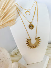 Load image into Gallery viewer, Flat lay of three layered 24K gold chain necklaces one with gold crescent charm, and two with gold sun burst pendant.
