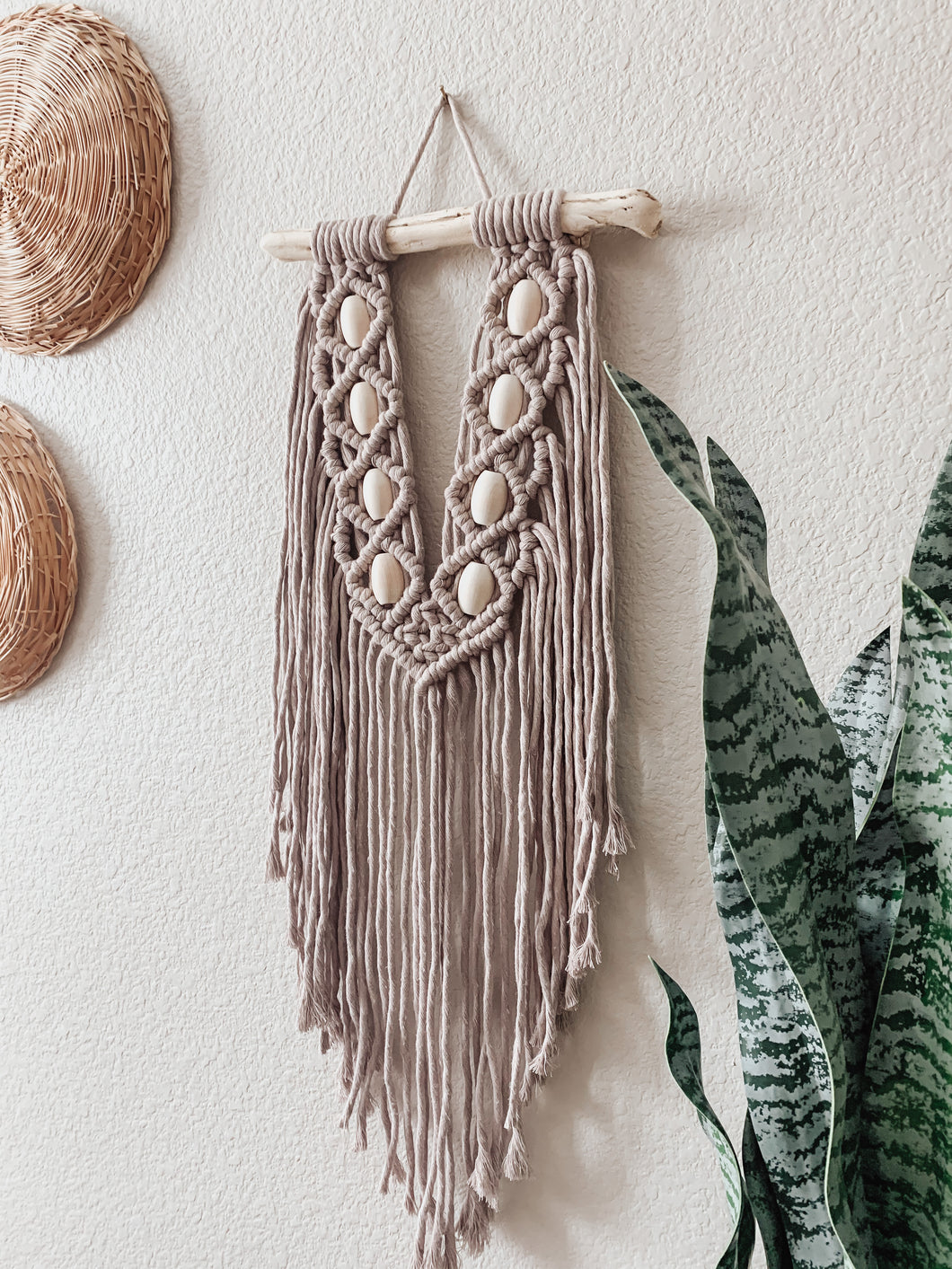 A macrame wall hanging made up of cotton cord hand knotted on local driftwood and accessorized with wood beads 